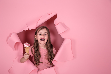 funny little girl peeking out of the hole with ice cream in her hands, on a colored pink background, space for text, Studio shootingの写真素材