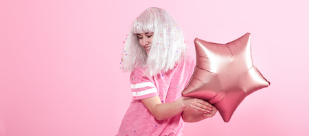 Funny Girl with silver hair gives a smile and emotion on pink background. Young woman or teen girl with balloons and confetti. Concept of holiday and party.の写真素材