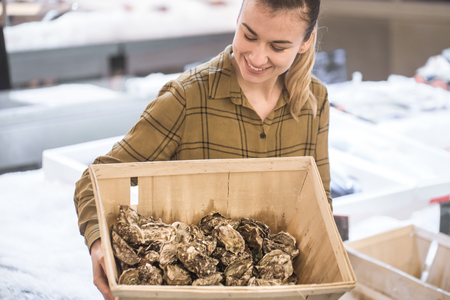 Woman in the supermarket with oysters. Beautiful young woman is holding a large box of oysters. The concept of healthy eating. Seafoodの写真素材