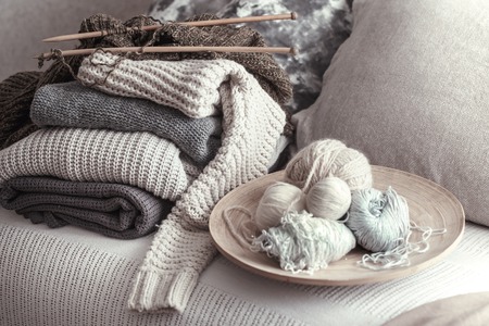 Vintage wooden knitting needles and threads for knitting on a cozy sofa with pillows and sweaters. Still life photo. The concept of comfortの写真素材