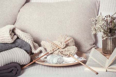 Vintage wooden knitting needles and threads on a cozy sofa with pillows and a vase of flowers. Open book for reading. Still life photo. The concept of comfortの写真素材