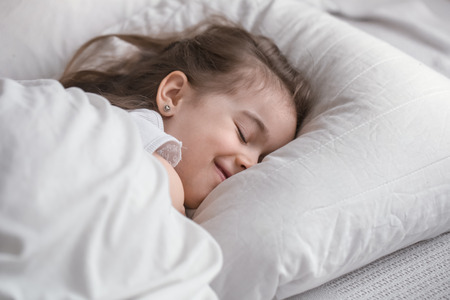 Cute little girl sleeps sweetly in a white cozy bed, the concept of children's rest and sleepの写真素材