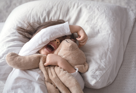 Cute little girl sleeps sweetly in a white cozy bed with a soft bear toy, the concept of children's rest and sleepの写真素材