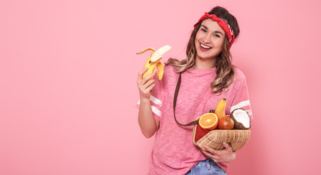 Horizontal portrait of hipster girl in stylish clothes , with healthy food, fruits, on pink background, lifestyle conceptの写真素材