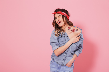 Horizontal portrait of hipster girl in jeans clothes with tattoo on body, on pink background, lifestyle conceptの写真素材