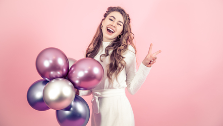 Young girl with beautiful balls on a colored pink background, dressed in a white dress, the concept of women's day and holidayの写真素材