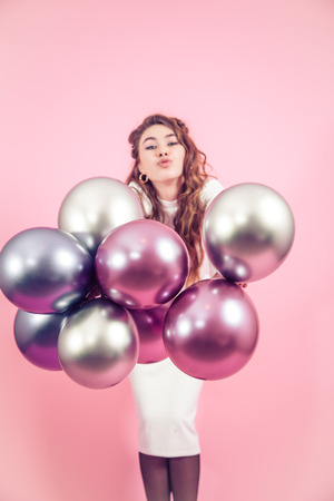 Young girl with beautiful balls on a colored pink background, dressed in a white dress, the concept of women's day and holidayの写真素材