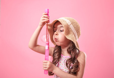 little girl in summer hat, blowing bubbles , on colored pink background, kids and summer concept