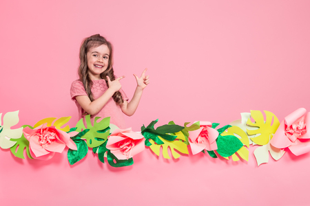 Portrait of a little girl on a summer pink background with paper flowers, place for text, summer advertising conceptの写真素材