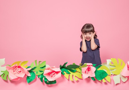 Portrait of a little girl on a summer pink background with paper flowers, place for text, summer advertising conceptの写真素材