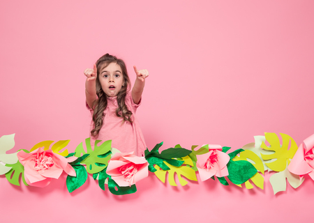 Portrait of a little girl on a summer pink background with paper flowers, place for text, summer advertising conceptの写真素材