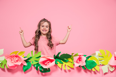 Portrait of a little girl on a summer pink background with paper flowers, place for text, summer advertising conceptの写真素材