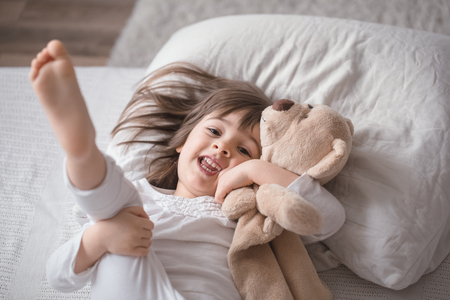 Cute little girl sleeps sweetly in a white cozy bed with a soft bear toy, the concept of children's rest and sleepの写真素材