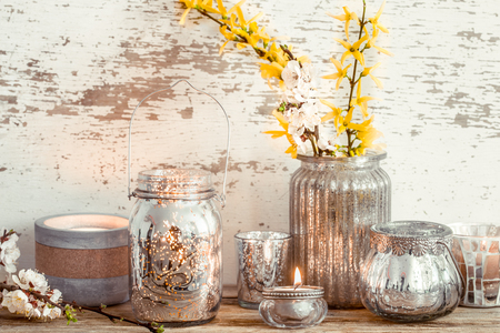 Home cozy beautiful decor, different vases and candles with spring flowers , on a wooden background , the concept of interior detailsの写真素材