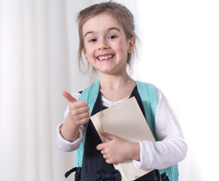 Girl-elementary school student with a backpack and a book on a light background .The concept of education and primary schoolの写真素材