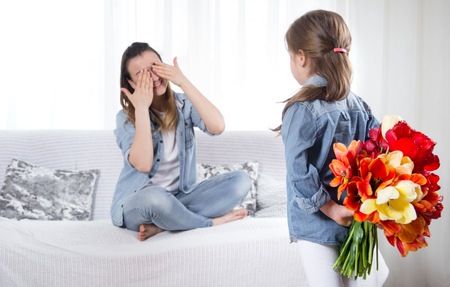 Happy mother's Day. Little sweet daughter with a large bouquet of tulips congratulates her mother. In the interior of the living room, the concept of a happy family lifeの写真素材