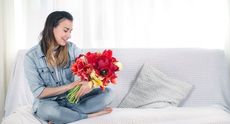 A young girl with a large bouquet of tulips sitting on the couch in the living room .の写真素材
