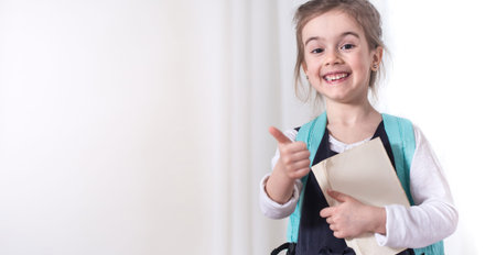 Girl-elementary school student with a backpack and a book on a light background .The concept of...