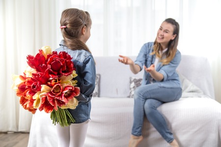 Happy mother's Day. Little sweet daughter with a large bouquet of tulips congratulates her mother. In the interior of the living room, the concept of a happy family lifeの写真素材