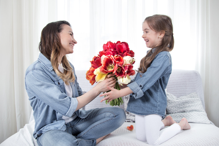 Happy mother's Day. Little sweet daughter with a large bouquet of tulips congratulates her mother. In the interior of the living room, the concept of a happy family lifeの写真素材