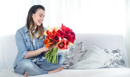 A young girl with a large bouquet of tulips sitting on the couch in the living room .の写真素材