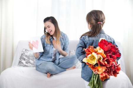Happy mother's Day. Little sweet daughter with a large bouquet of tulips congratulates her mother. In the interior of the living room, the concept of a happy family lifeの写真素材