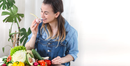 Young and happy woman eating salad at the table ,on a light background in denim clothes. The concept of a healthy home-made food. Place for text .の写真素材