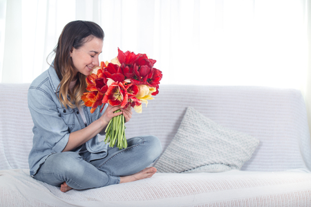 A young girl with a large bouquet of tulips sitting on the couch in the living room .の写真素材
