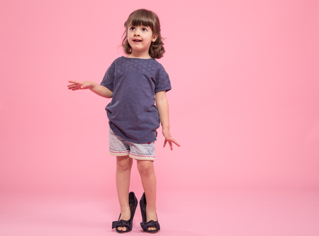 Funny little girl is a fashionista in the shoes of the mother , the concept of children's fashionの写真素材
