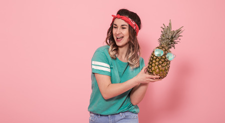 Horizontal portrait of hipster girl in stylish clothes, and pineapple in sunglasses, on pink background, lifestyle conceptの写真素材