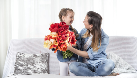 Happy mother's Day. Little sweet daughter with a large bouquet of tulips congratulates her mother. In the interior of the living room, the concept of a happy family lifeの写真素材