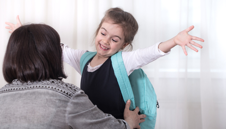 Parent and girl elementary school student hugging each other on a light background . Back to school conceptの写真素材