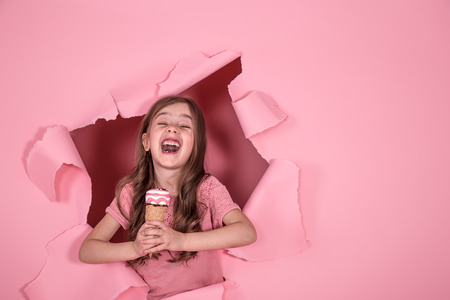 funny little girl peeking out of the hole with ice cream in her hands, on a colored pink background, space for text, Studio shootingの写真素材