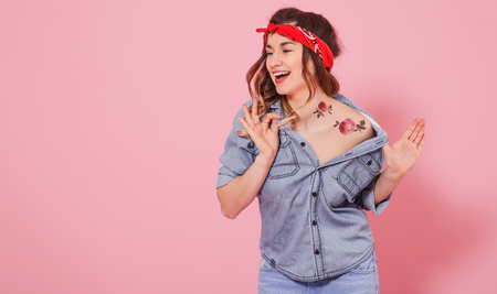 Horizontal portrait of hipster girl in jeans clothes with tattoo on body, on pink background, lifestyle conceptの写真素材