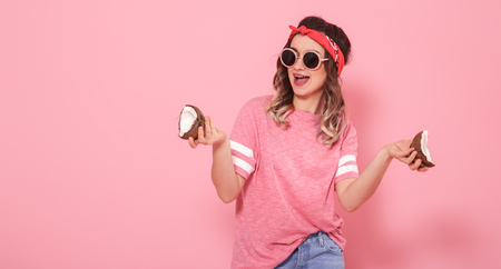 Horizontal portrait of hipster girl in stylish clothes with sunglasses, coconuts in her hands, on a pink background, lifestyle conceptの写真素材