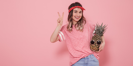 Horizontal portrait of hipster girl in stylish clothes, with pineapple in sunglasses, on pink background, lifestyle conceptの写真素材