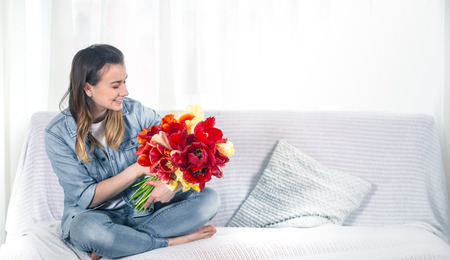 A young girl with a large bouquet of tulips sitting on the couch in the living room .の写真素材