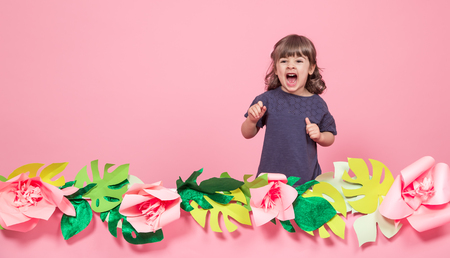 Portrait of a little girl on a summer pink background with paper flowers, place for text, summer advertising conceptの写真素材
