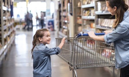 Mother and daughter in blue shirts shopping in supermarket using cartの写真素材