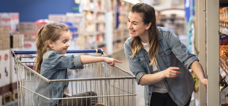 Mother and daughter in blue shirts shopping in supermarket using cartの写真素材