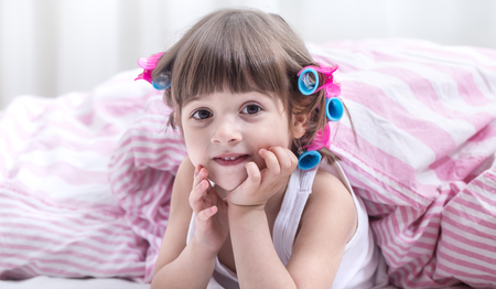 Cute little girl smiling while lying in a cozy white bed with , the concept of children's rest and sleepの写真素材