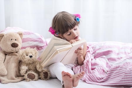 Cute little girl smiling while lying in a cozy white bed with , the concept of children's rest and sleepの写真素材
