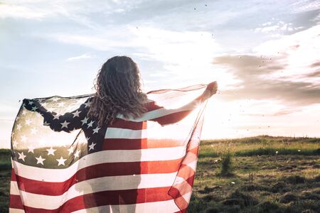 Young happy girl running and jumping carefree with open arms over wheat field. Holding USA flag. Toned image. Selective focus.の写真素材