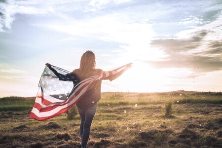 Young happy girl running and jumping carefree with open arms over wheat field. Holding USA flag. Toned image. Selective focus.の写真素材
