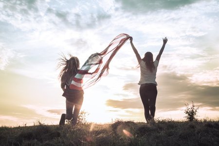 Young happy girl running and jumping carefree with open arms over wheat field. Holding USA flag....