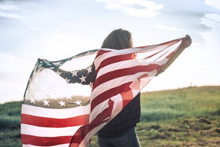 Young happy girl running and jumping carefree with open arms over wheat field. Holding USA flag. Toned image. Selective focus.の写真素材