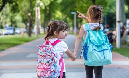 Back to school education concept with girl kids, elementary students, carrying backpacks going to class on school first day holding hand in hand together walking up building stair happilyの写真素材