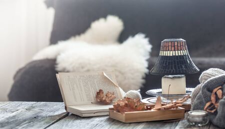 Autumn - winter still Life in a homely atmosphere with decorative items in the living room . With lamp on wooden table , book and autumn leaves .の写真素材