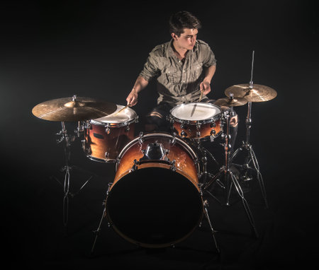 Professional drummer playing on drum set on stage on the black background with drum sticks and...