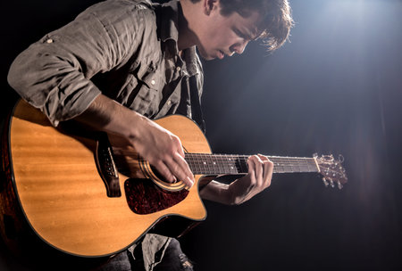 Guitarist, music. A young man plays an acoustic guitar on a black isolated background. Pointed light